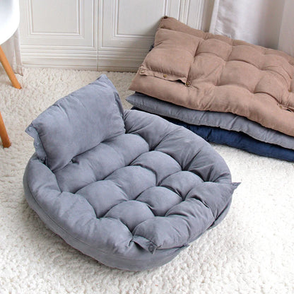 Grey pet bed on a white carpet with folded blankets in the background